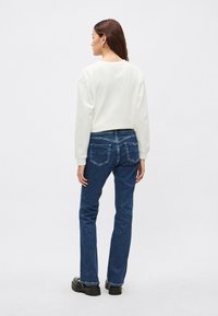 Sudadera blanca de manga larga, combinada con vaqueros azul oscuro de pierna recta con bolsillos traseros y costuras sutiles. Zapatos plataforma negros.