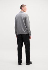 Grauer Strickpullover mit Kragen, kombiniert mit dunklen, strukturierten Hosen. Das Outfit betont eine lässige Passform mit subtilen Details.