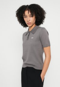 Szürke rövid ujjú galléros póló bordázott gallérral, kis hímzett "2ND" logóval. Puha, könnyű kötött anyagból készült.