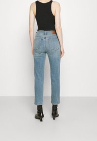 Jeans de mezclilla azul claro con un corte relajado, cintura alta y bolsillos delanteros y traseros. Combinados con una blusa negra sin mangas y botas de tacón.
