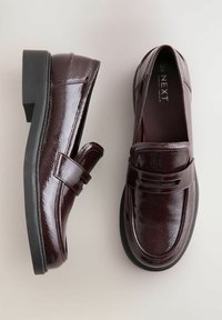 Burgundi värvi lakknahast loafers'id ümarate varvastega, peene rihma detailiga ja mustast kummist tallaga. Sile tekstuur läikiva viimistlusega.