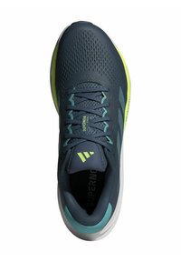 Dunkelblaue Sportschuhe mit perforiertem Obermaterial, grünen Akzenten, strukturierten Schnürsenkeln und weißer Sohle. Mit Branding auf der Zunge.