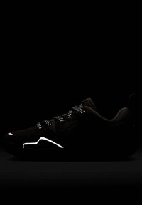 Czarne sportowe buty z teksturowaną siateczkową cholewką, odblaskowymi sznurowadłami z detalami i białym akcentem wzdłuż podeszwy. Ciemne tło podkreśla cechy buta.