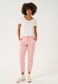 Lightweight, fitted white t-shirt, paired with pastel pink, tapered pants featuring a front button closure, and worn with white sneakers.