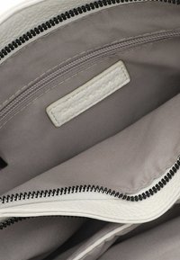 White leather bag interior with a smooth, gray fabric lining. Features a zippered compartment and a white textured label. Black zipper detail.