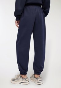 Pantaloni da tuta blu navy realizzati in tessuto morbido, con vita elastica e caviglie cuffs, abbinati a sneakers chiare.