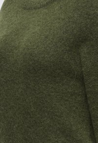 Gros plan sur un tissu doux et duveteux de couleur vert olive uni, montrant clairement la texture et les fibres.
