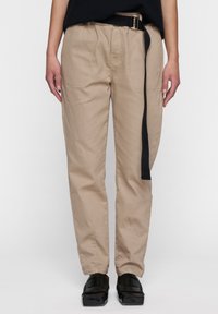 Beige, lichtgewicht katoenen broek met een ontspannen pasvorm, voorzien van een zwarte riemdetail en zijzakken. Gladde textuur en gestikte accenten.