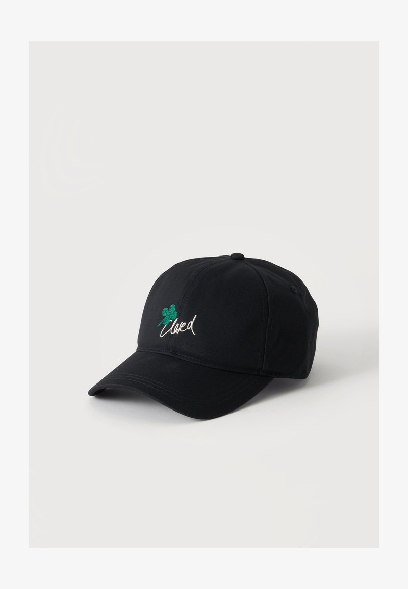 Casquette de baseball noire avec un trèfle vert à quatre feuilles et un texte blanc en cursive à l'avant, présentée sur un fond clair uni.