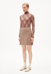 Langärmliges, figurbetontes Oberteil in Beige mit braunem Karomuster; kombiniert mit einem beigefarbenen Cord-Minirock mit einem Schlitz vorne. Weiße Schuhe und Socken.