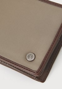 Braune Textiltasche mit glatter Oberfläche, ausgestattet mit einem runden silbernen Hardware-Akzent und sauberem Stich entlang der Kanten.