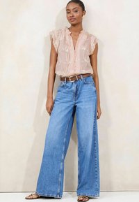 Peach sheer blouse with floral embroidery and ruffled sleeves, paired with wide-leg blue denim jeans and a brown belt. Sandals included.