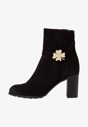 Schwarze Wildleder-Stiefelette mit Blockabsatz, die mit einem goldenen Blumenakzent und einer glatten Textur versehen ist. Mit seitlichem Reißverschluss für ein einfaches An- und Ausziehen.