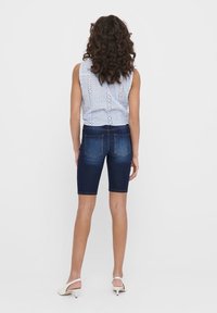 Bermuda en jean bleu foncé avec une coupe ajustée sur les hanches et des poches arrière. Associé à un haut sans manches bleu clair avec des détails en œillets.