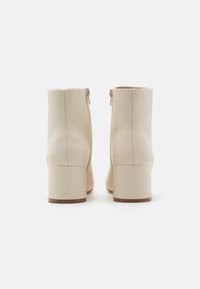 Bottines beige en cuir lisse, dotées d'une fermeture éclair latérale et d'un talon bloc. Bout arrondi et détails de couture nets.