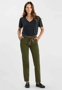 Pantalon vert olive avec une ceinture nouée imprimé léopard, associé à un t-shirt noir à col en V, offrant une coupe décontractée et une texture lisse.
