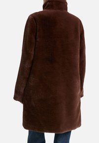 Brauner Kunstpelzmantel mit hohem Kragen, mit glatter Textur und lockerer Passform. Der Mantel reicht bis zur Mitte der Oberschenkel und hat keine sichtbaren Verschlüsse.