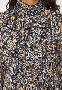 Blusa con motivo floreale in blu navy, bianco e arancione, con un collo alto a volant, dettagli con bottoni e tessuto testurizzato.