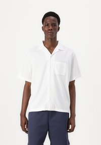 White short-sleeved button-up shirt made of lightweight fabric, featuring a pocket and a relaxed fit. Smooth texture and classic collar design.