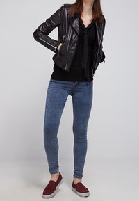 Svart läderbikerjacka med silverfärgade dragkedjor, åtsittande svart topp, blå skinny jeans och bordeauxiga slip-on skor med texturerat tyg.