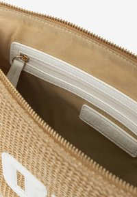 Pochette tissée couleur tan avec un extérieur texturé, présentant une poche zippée blanche et une étiquette de marque à l'intérieur. Fermeture zippée dorée en haut.