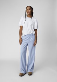 Haut à manches courtes côtelé blanc et pantalon large bleu clair, associé à des sabots marron avec des accents argentés. Texture lisse, coupe décontractée.