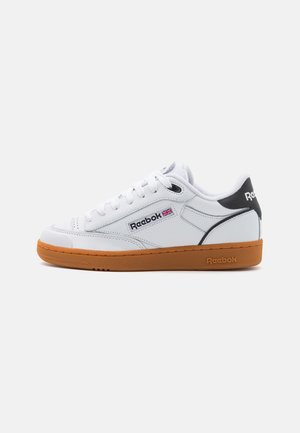White leather sneakers with a gum rubber sole. Features a black heel accent and Reebok logo on the side, flat laces, and rounded toe.