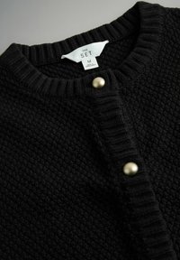 Sort struktureret cardigan med ribbet krave og manchetter, lukket med runde knapper i guldfarve, mærket "THE SET" størrelse M.
