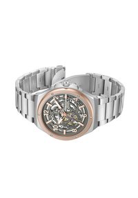 Reloj de acero inoxidable plateado con bisel dorado rosado, esfera transparente y movimiento visible; presenta números grandes y una pulsera de eslabones metálicos.