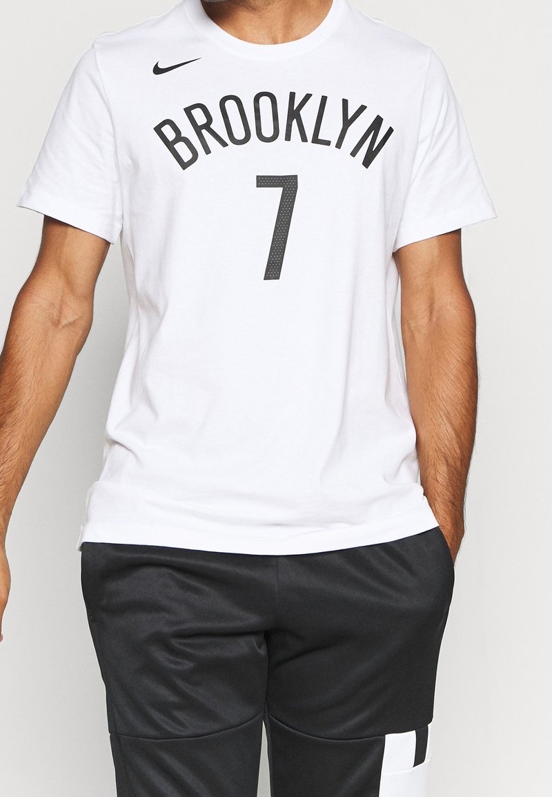 Valkoinen Nike T-paita, jossa on rohkea musta teksti "BROOKLYN" ja numerot "7" alla, standardi pyöreä kaula-aukko, lyhyet hihat.