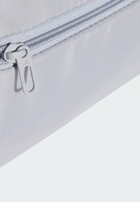 Harmaasta teksturoidusta kankaasta valmistettu laukku, jossa on sileä hopeanvärinen vetoketju ja vetotappi. Sisältää vetoketjullisen taskun, korostaen toiminnallista muotoilua ja kestävyyttä.