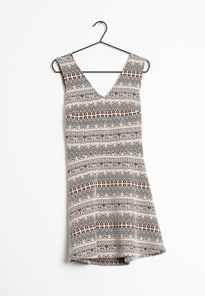 Robe sans manches avec décolleté en V sur un cintre noir, présentant un motif tribal géométrique beige, noir et marron.
