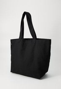 Svart tote bag laget av slitesterkt stoff. Har to robuste håndtak og et romslig, åpent design uten synlige beslag eller mønstre.