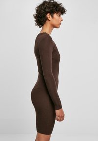 Abito lungo a maniche lunghe marrone a coste con silhouette aderente, taglio a ginocchio e tessuto testurizzato, mostrato in profilo laterale.