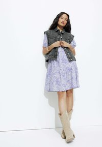 Gilet en denim sur une robe violette à motifs floraux ; bottes beiges jusqu'aux genoux avec une texture douce et une forme de style Western.