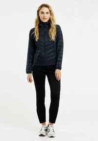 Námornícka puffer bunda s vysokým golierom, prešívaný dizajn, dlhé rukávy; kombinovaná s čiernymi legínami a športovými topánkami s multicolor akcentmi.