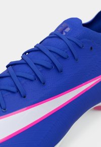 Μπλε αθλητικό παπούτσι με υφή στην επάνω επιφάνεια, επίπεδα κορδόνια, λευκές και ροζ λεπτομέρειες στο πλάι και αεροδυναμικό, κωνικό σχήμα.