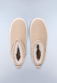 Stivaletti beige senza lacci con una morbida fodera in pelliccia, materiale in pelle liscia, punta arrotondata e un sottile dettaglio di cucitura decorativa. Suola bianca morbida.