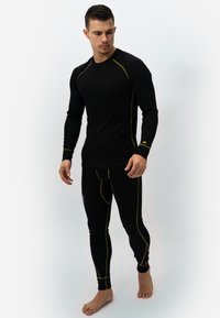 Zwarte thermische top met lange mouwen en aansluitende leggings met gele stiksels. Gemaakt van rekbaar materiaal voor comfort en warmte.