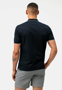 Polo shirt blu navy a maniche corte, con colletto sottile e spacchi laterali, abbinato a pantaloni corti a righe. Finitura in tessuto testurizzato.