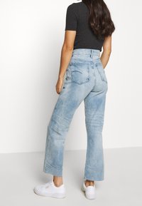 Ljusblå högmidjade jeans med rak ben, urtvättad textur och två bakfickor; kombinerat med vita sneakers och en svart ribbad topp.