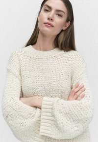 Crème gebreide sweater met een losse pasvorm, voorzien van een gestructureerd, open geweven patroon en brede, ribgebreide manchetten. Lichtgewicht en ademend materiaal.