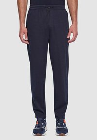 Pantaloni jogger blu navy con vita elastica e coulisse, dotati di tasche laterali e design con gamba affusolata. Tessuto morbido ed elastico.
