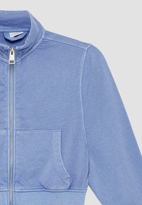Helles blaues Reißverschlussjackett aus weichem Stoff, mit Stehkragen, frontalen Taschen und geripptem Saum sowie Bündchen.