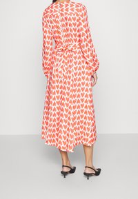 Robe maxi avec un motif cœur orange et blanc, à manches longues, taille cintrée et détail à nouer à l'arrière.