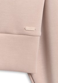 Tissu rose clair en gros plan montrant une couture pliée et une petite étiquette rectangulaire de la marque 4F cousue sur le vêtement.