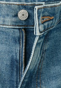 Nahaufnahme von blauen Jeans aus Denim mit teilweise geöffnetem Metallreißverschluss und Metallknopf mit der Aufschrift "MNG Denim". Auffällige orangefarbene Nähte sichtbar.