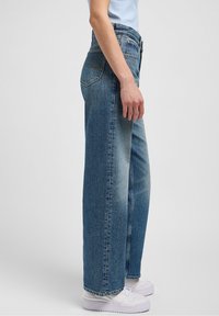 Light blue denim jeans with a straight leg design, featuring a high waist, back pocket detail, and subtle fade texture.