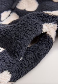 Tissu en fausse fourrure bleu foncé avec des pois crème, présentant une surface douce et texturée ainsi que des plis. Montre des détails de couture et de design complexes.