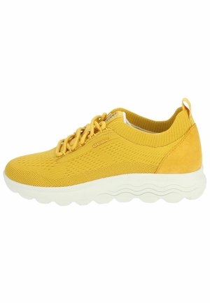 Chaussure de sport jaune en maille et daim, avec une semelle blanche arrondie, un design à lacets et des accents texturés sur le dessus.